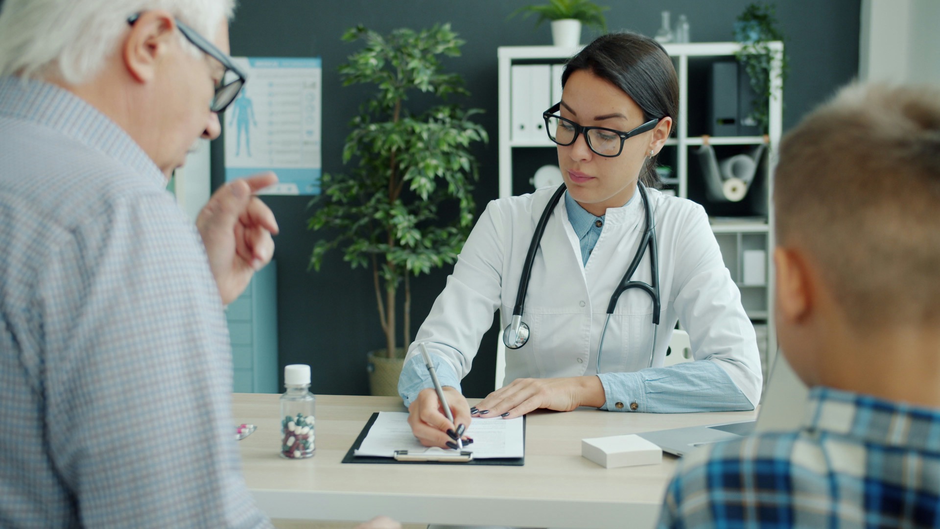 A doctor reviewing a patient's paperwork with a family in a clinical office, the kind of case Synthis helps process.